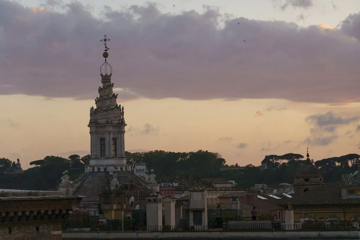 The spiral lantern of Sant'Ivo alla Sapienza rising above Rome's rooftops against a pink and amber evening sky